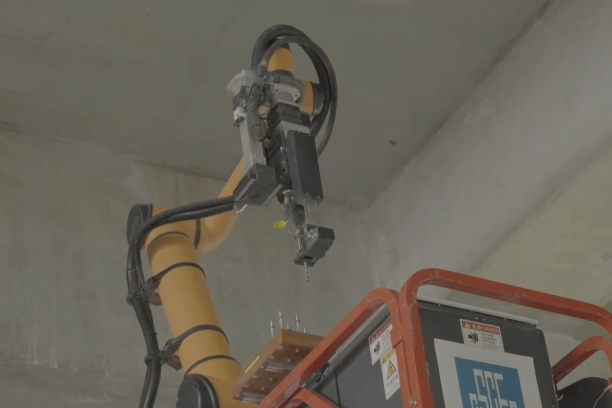 Robotic arm drilling overhead concrete inside a building under construction.